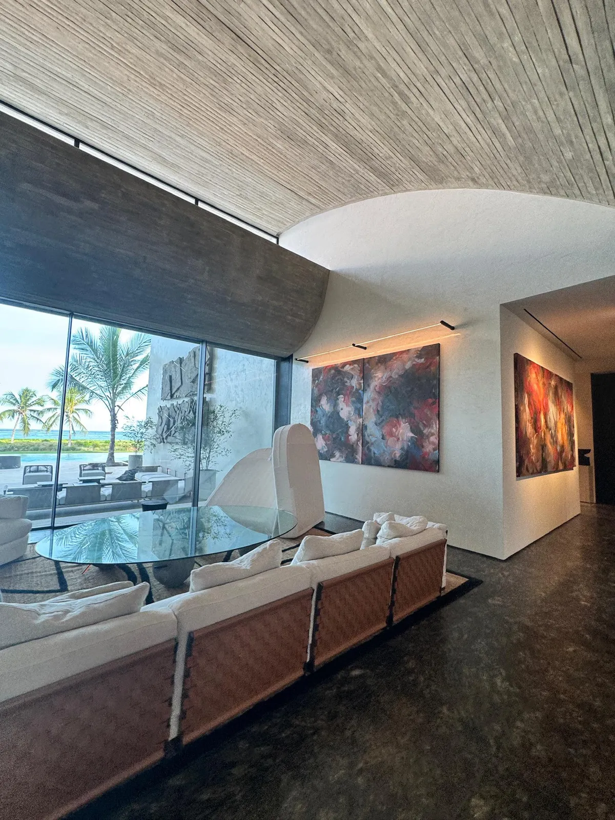 Living room with accent-lit abstract paintings and floor-to-ceiling windows facing the pool and ocean