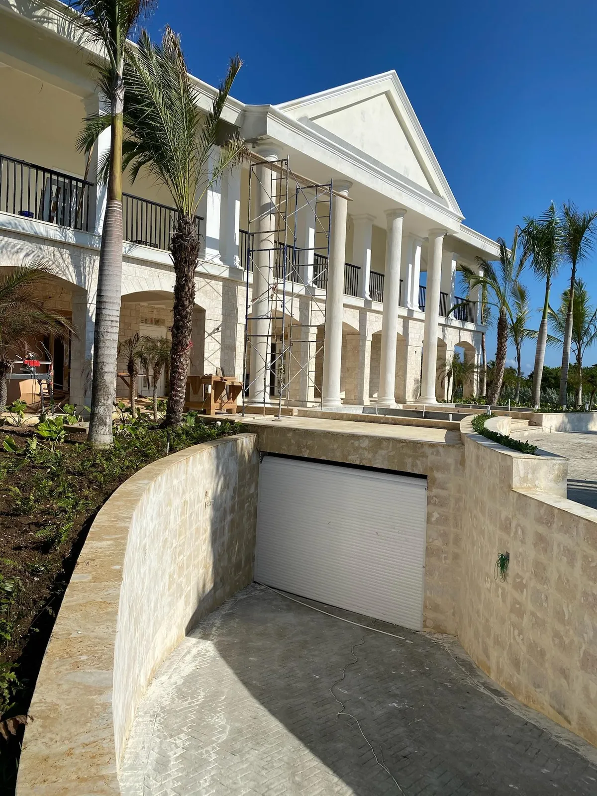 Underground garage entrance with a white roll-up door below a columned colonial villa during construction