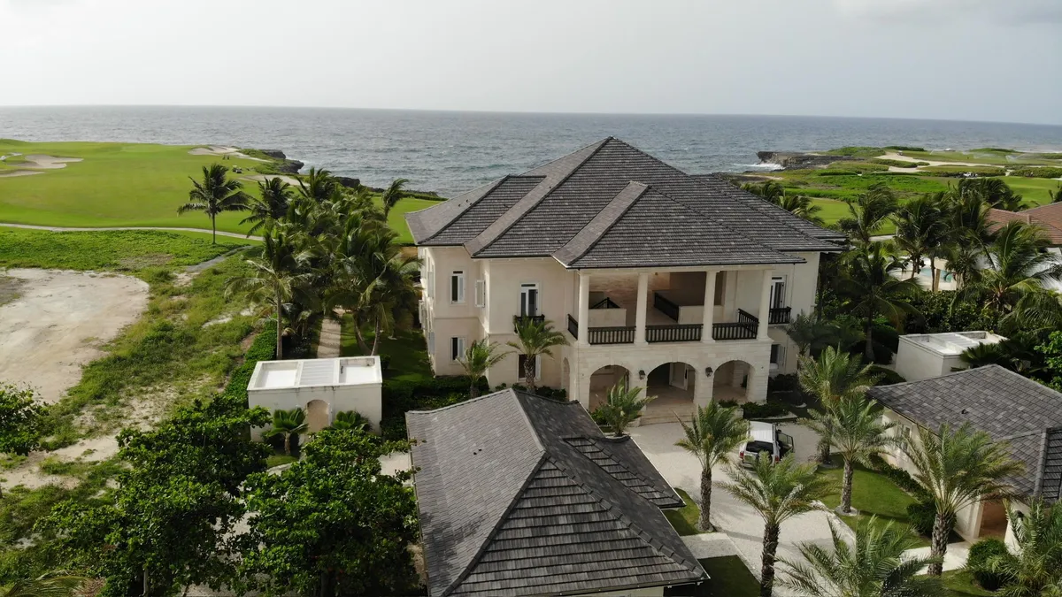 Aerial view of a two-story colonial-style villa beside a golf course, with the ocean beyond