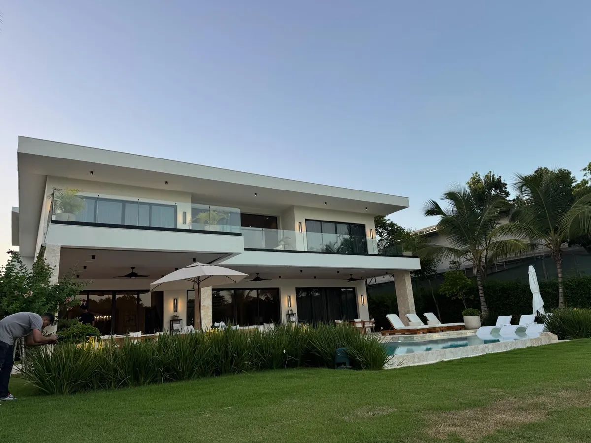 Rear facade of a contemporary two-story villa with glass balconies, pool and lawn at dusk