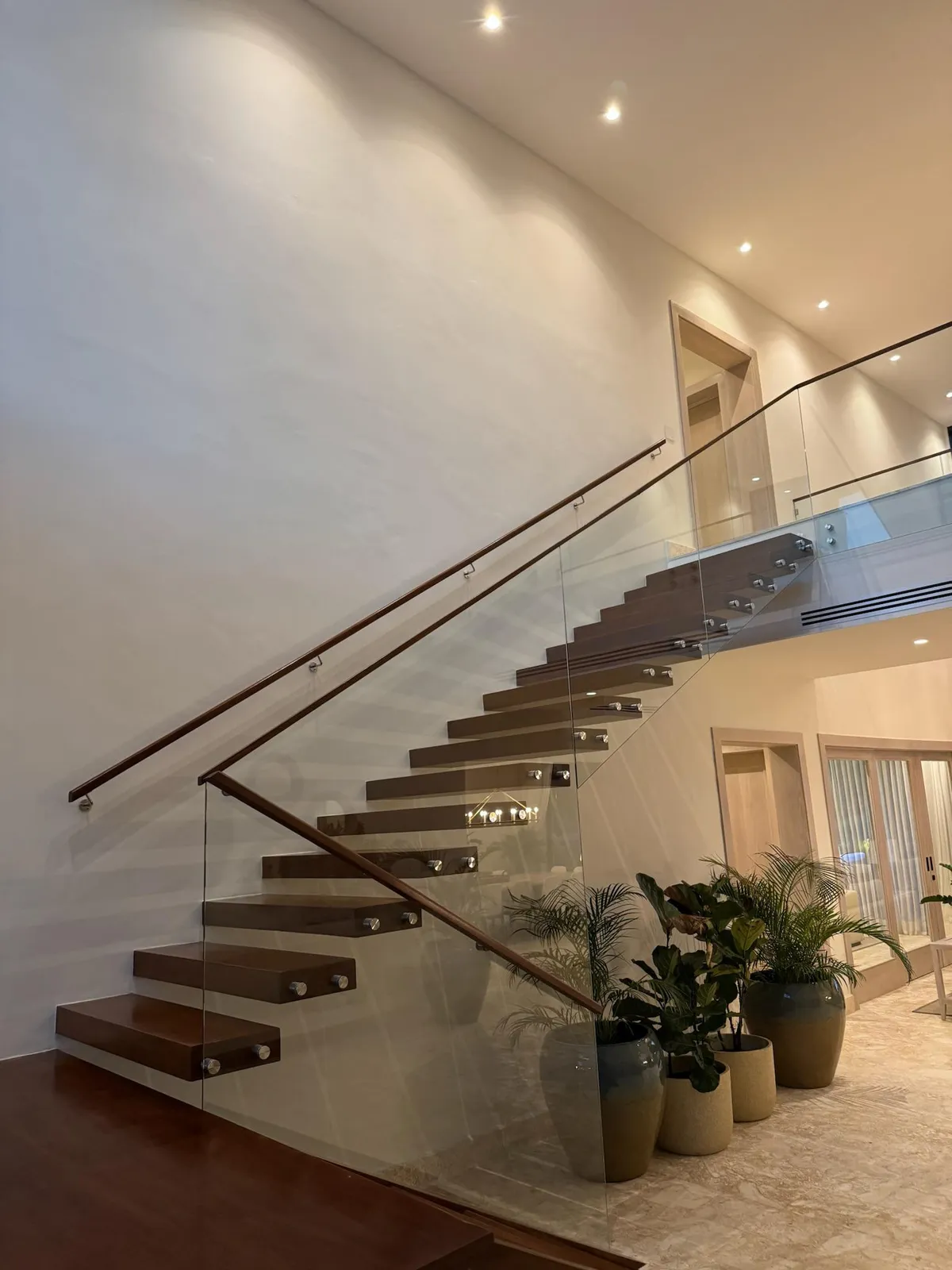 Floating wooden staircase with a glass balustrade beneath recessed downlights